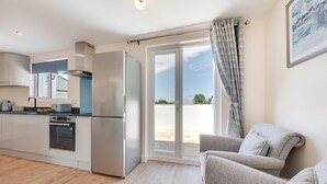 A modern kitchen with stainless steel appliances, a dining area with a grey sofa, and a large sliding glass door leading to an outdoor patio. - 3 Bed in Higher Crackington (oc-avond) (Crackington Haven)