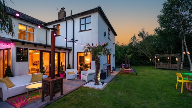 Ein zweistöckiges Haus mit Terrasse, Sitzgelegenheit im Freien und einem Garten.