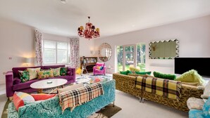 Ein Wohnzimmer mit einem violetten Sofa, einem blau gemusterten Sofa und einem gelben Sofa. Es gibt eine Chandelier, ein Bücherregal und einen großen Spiegel an der Wand.