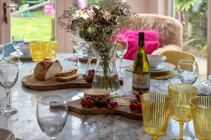 A dining table set with a bottle of wine, a vase with flowers, and various food items. - 5 Bed in Dunstan (oc-588874) (Dunstan)
