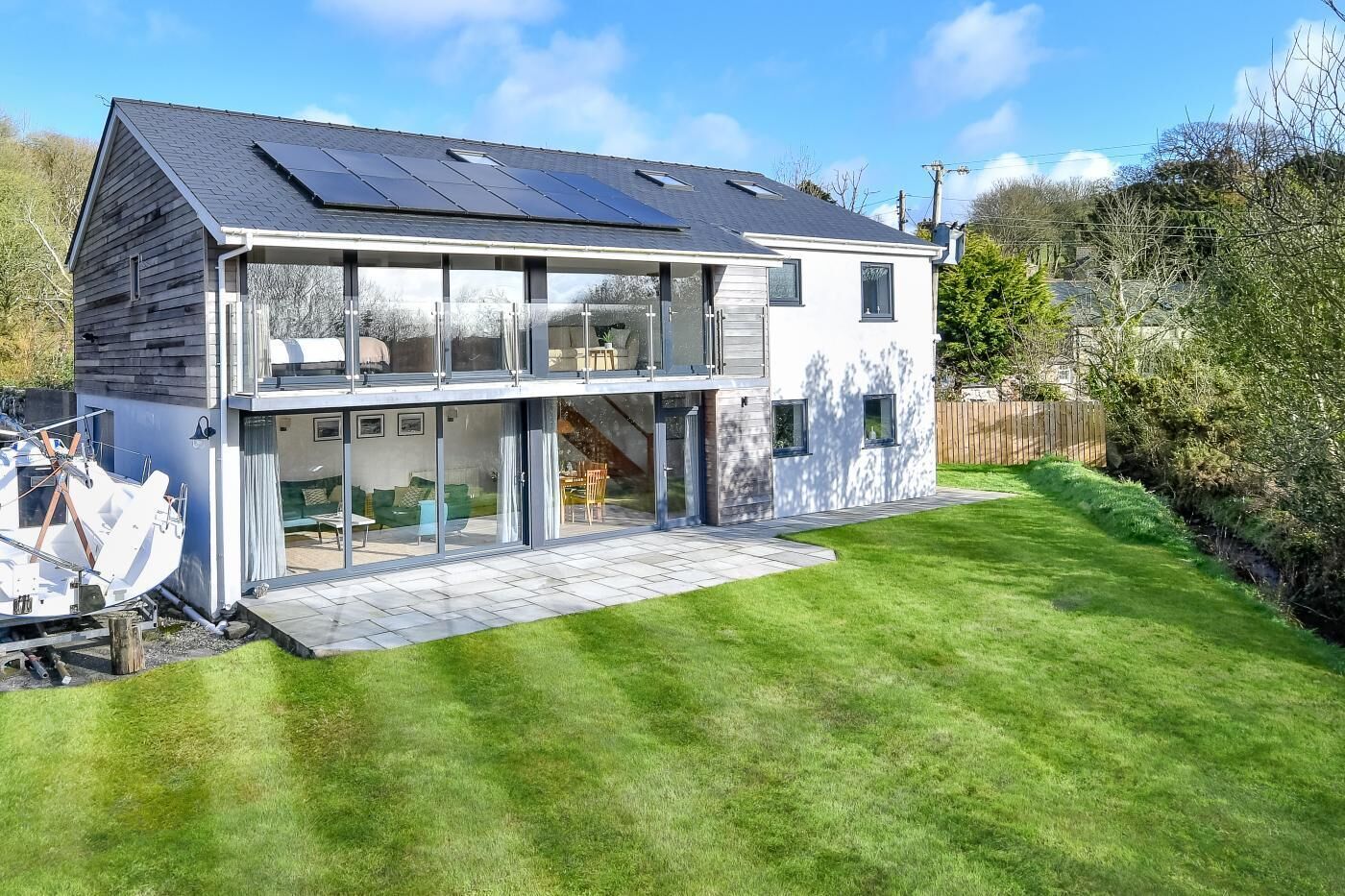 Een modern huis met twee verdiepingen, grote ramen, een dak met zonnepanelen en een verzorgd gazon.