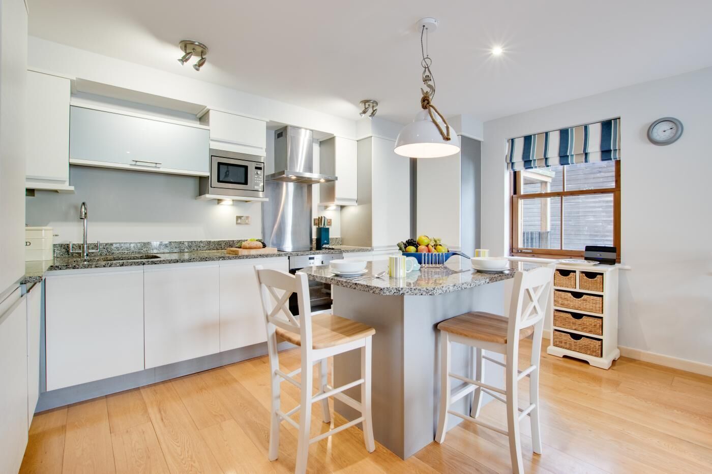A modern kitchen with white cabinets, a granite countertop, a central island with bar stools, stainless steel appliances, and a hanging light fixture.