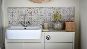 Une salle de bain avec un lavabo blanc, des carreaux décoratifs, un miroir rond et une petite plante en pot.
