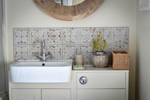 A bathroom with a white sink, decorative tiles, a round mirror, and a small potted plant. - 2 Bed in Pwllheli (oc-30aber) (Pwllheli)