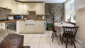 Een moderne keuken met een stenen muur, een eethoek met een tafel en stoelen, en een gezellige zithoek met een fauteuil bekleed met vacht.