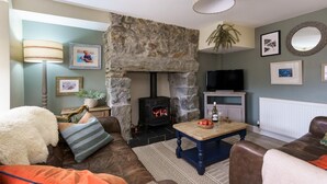 Een gezellige woonkamer met een stenen openhaard, comfortabele zitplaatsen en een televisie.
