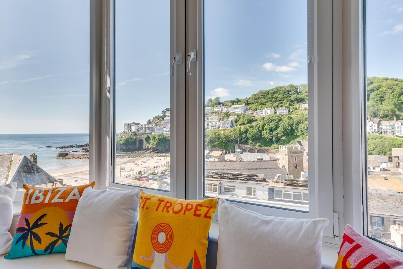 A room with large windows overlooking a beach and historic buildings.