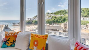 A room with large windows overlooking a beach and historic buildings. - 1 Bed in Looe (oc-seahol) (Looe)
