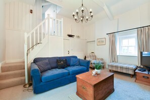 A living room with a blue sofa, a wooden coffee table, a staircase, and a chandelier.