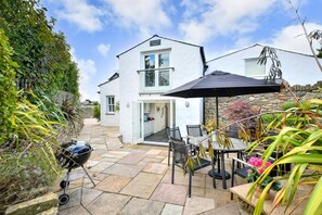 A two-story house with a patio area featuring a grill, outdoor seating, and a stone wall.