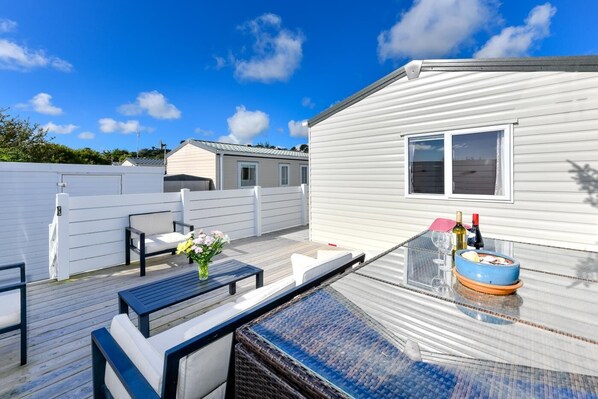A deck with outdoor furniture, a dining table, and a small table with drinks.