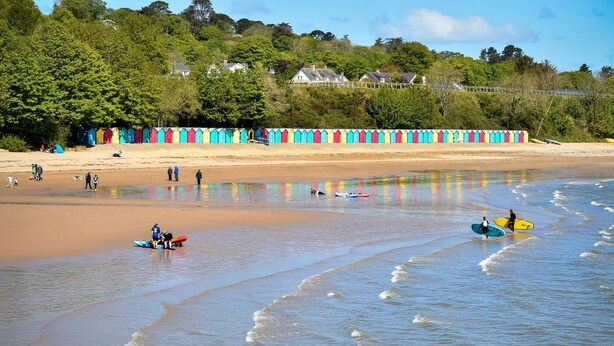 A beach with colorful beach huts, a sandy shore, and people in the water. - 3 Bed in Llanbedrog (oc-brntr) (Llanbedrog)