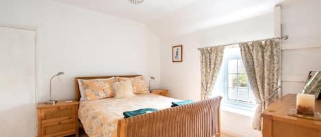 Un dormitorio con cama, mesitas de noche, lámpara, cómoda y ventana con cortinas.