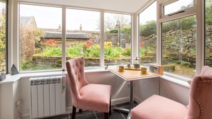 Una habitación con un gran ventanal, un radiador, una mesa con un radio y dos sillas rosas.
