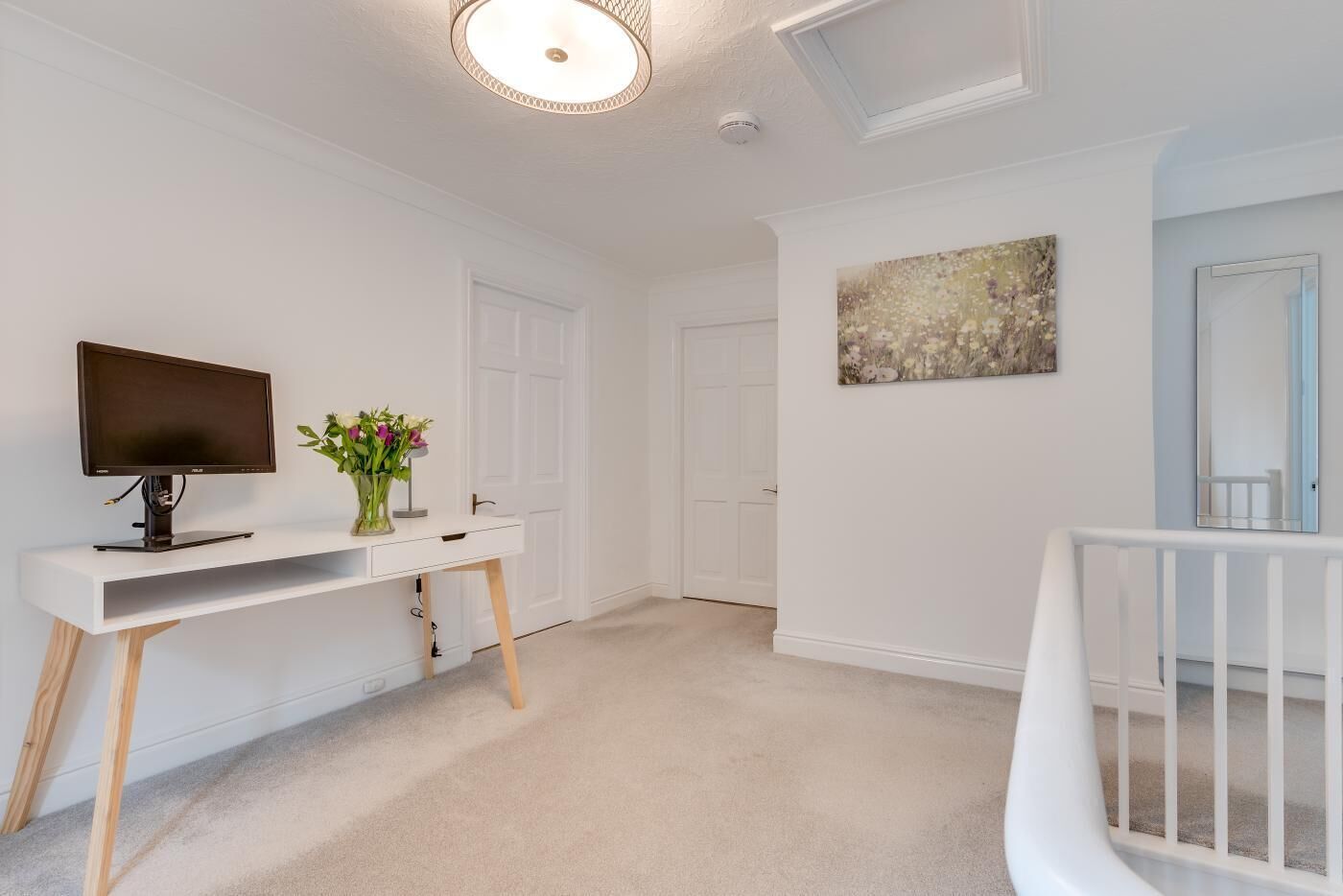 A modern, clean room with a white desk, a flat-screen TV, and a vase of flowers.