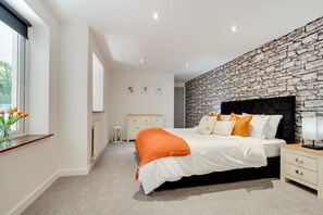 A bedroom with a stone wall, a bed with white and orange bedding, a nightstand, and a window with flowers. - 1 Bed in Carmarthen (oc-waw218) (Carmarthen)