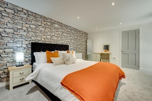 Ein Schlafzimmer mit Steinsandsteinwand, einem Bett mit weißer Bettwäsche und orangefarbenen Akzenten, einem Nachttisch mit Lampe und einer Tür.
