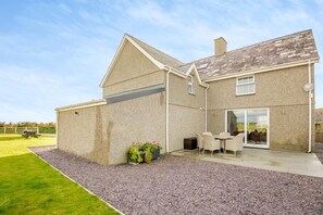 A two-story house with a patio area, a small garden, and a gravel driveway. - 4 Bed in Rhoshirwaun (oc-bow324) (Rhoshirwaun)