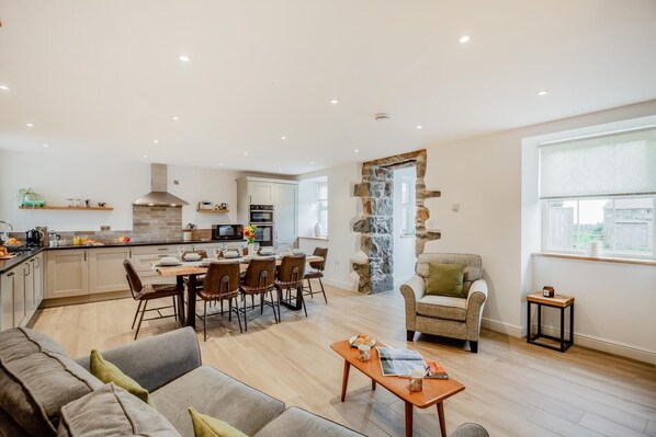 A modern kitchen with a dining area, a stone feature wall, and a cozy seating area with a sofa and a chair. - 4 Bed in Rhoshirwaun (oc-bow324) (Rhoshirwaun)