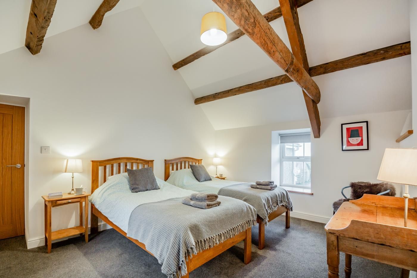 A room with two wooden beds, a wooden table, a window, and a ceiling with exposed beams.