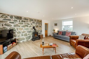 A cozy living room with a stone wall, a fireplace, a television, a sofa, and leather chairs. - 4 Bed in Rhoshirwaun (oc-bow324) (Rhoshirwaun)