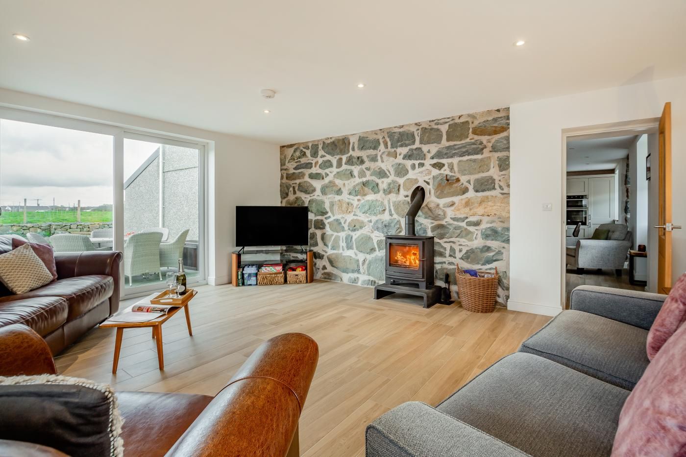 A cozy living room with a stone wall, a fireplace, a TV, and a dining area with a view.