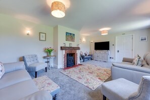A living room with a fireplace, sofas, a television, and a patterned rug. - 4 Bed in Great Plumstead (oc-2295) (Great Plumstead)