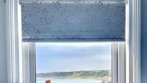 Un dormitorio con vista a un pueblo costero a través de una ventana con un adornado cortinero floral.
