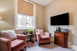 A living room with two armchairs, a small table with a plant and a vintage telephone, a television mounted on the wall, and a wooden cabinet with a laptop. - 3 Bed in Scarborough (oc-s113) (Scarborough)