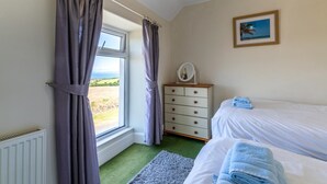 Un dormitorio con cama, cómoda, ventana con cortinas, alfombra verde y un cuadro enmarcado en la pared.