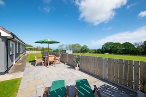 A patio with a table and chairs, a green umbrella, and a wooden fence. - 3 Bed in Aberaeron (oc-bow330) (Ciliau Aeron)