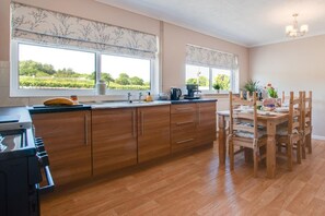 Une cuisine moderne avec des meubles en bois, un coin repas avec des chaises en bois et de grandes fenêtres agrémentées de stores décoratifs qui mettent en valeur la vue.