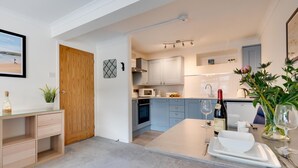 A modern kitchen with light blue cabinets, a wooden door, and a dining area with a white table set for two. - 1 Bed in West Looe (oc-1west) (Looe)