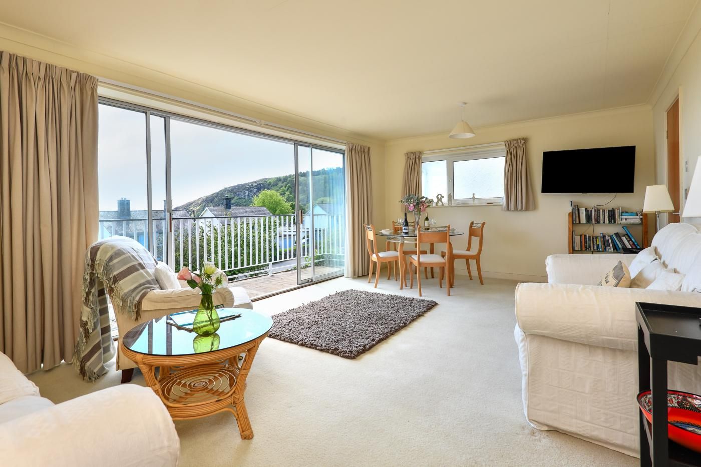 A spacious living room with a balcony, a dining area, and a TV mounted on the wall.