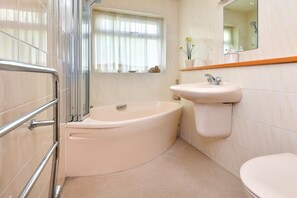 A bathroom with a bathtub, a sink, a toilet, a window with curtains, and a mirror. - 3 Bed in Llanbedrog (oc-gerddi) (Llanbedrog)