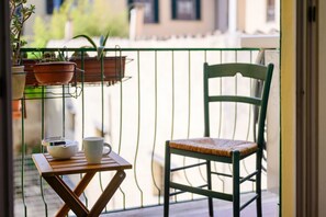 A balcony with a green chair, a small wooden table, and potted plants. - Sweet House in Macci Street (Firenze)