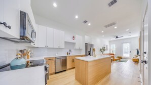 A modern kitchen with white cabinetry, a central island, and a dining area with a sofa and table. - Modern Retreat • Private Pergola • Pool • Fire Pit (Houston)