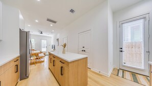 A modern kitchen with wooden cabinets, a central island, and a dining area with a table and chairs. - Modern Retreat • Private Pergola • Pool • Fire Pit (Houston)