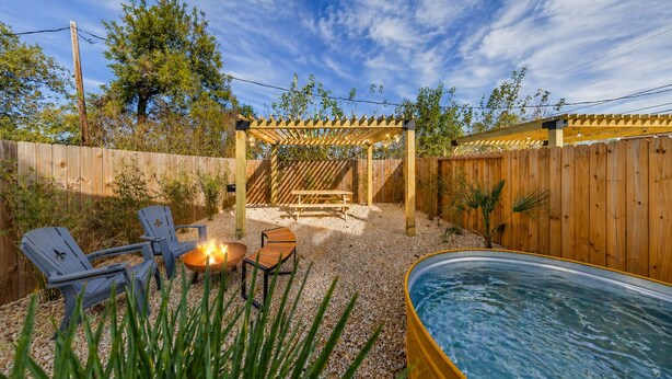 A backyard with a hot tub, two Adirondack chairs, a fire pit, and a wooden pergola. - Modern Retreat • Private Pergola • Pool • Fire Pit (Houston)