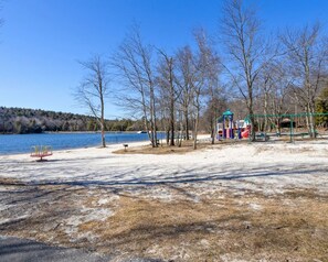 A lakeside park with a playground, benches, and a walking path.