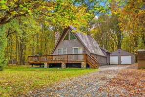 A cabin with a stone chimney, a wooden deck, and a garage.