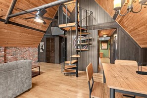 Habitación estilo loft con techo de madera, una escalera en espiral y un comedor con mesa y sillas.