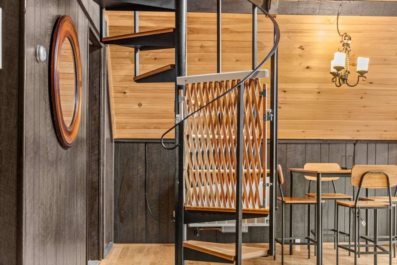A wooden interior with a spiral staircase, a wall-mounted light fixture, and a seating area with tables and chairs.