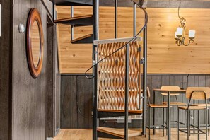 A wooden interior with a spiral staircase, a wall-mounted light fixture, and a seating area with tables and chairs.