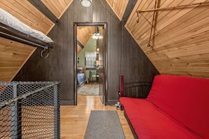 A room with a sloped ceiling, a bunk bed, a red sofa, and a small table with a chair.