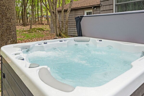 Un jacuzzi con múltiples chorros, rodeado de árboles y una casa al fondo.