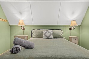 Quarto com cama, duas mesinhas de cabeceira, duas luminárias e uma toalha enrolada no chão.