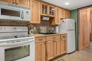 A kitchen with wooden cabinets, a stove, a microwave, a refrigerator, and a sink.