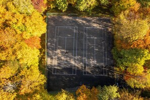 An aerial view of a tennis court surrounded by trees with autumn foliage.