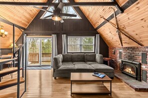 A cozy loft-style living room with a sectional sofa, a fireplace, and a wooden ceiling.